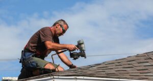 man nailing roof shingles