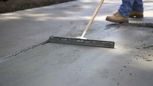 Man drags broom over wet concrete to give it a rough surface