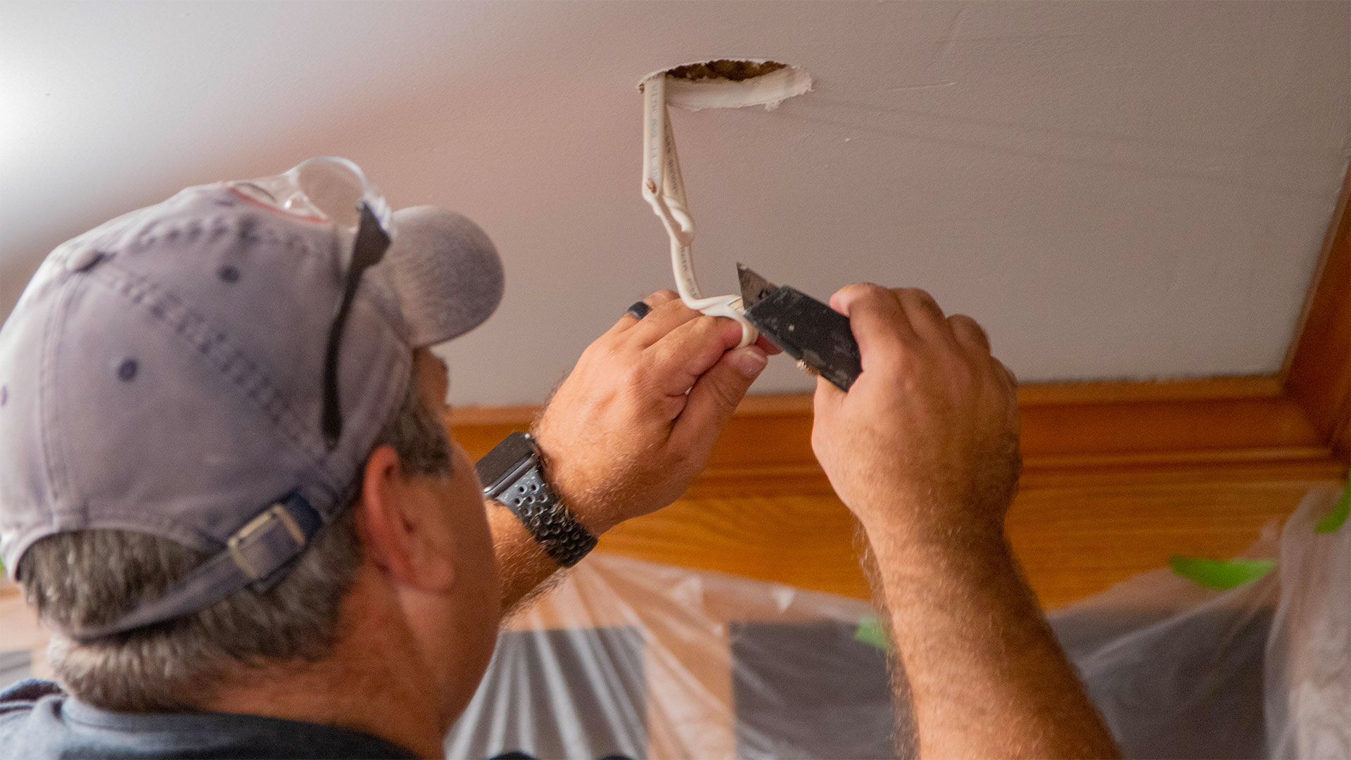 Man strips electrical wiring while installing a recessed light