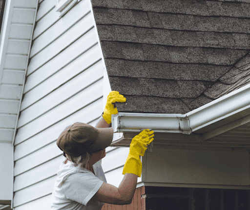 A person performing gutter maintenance on a home.